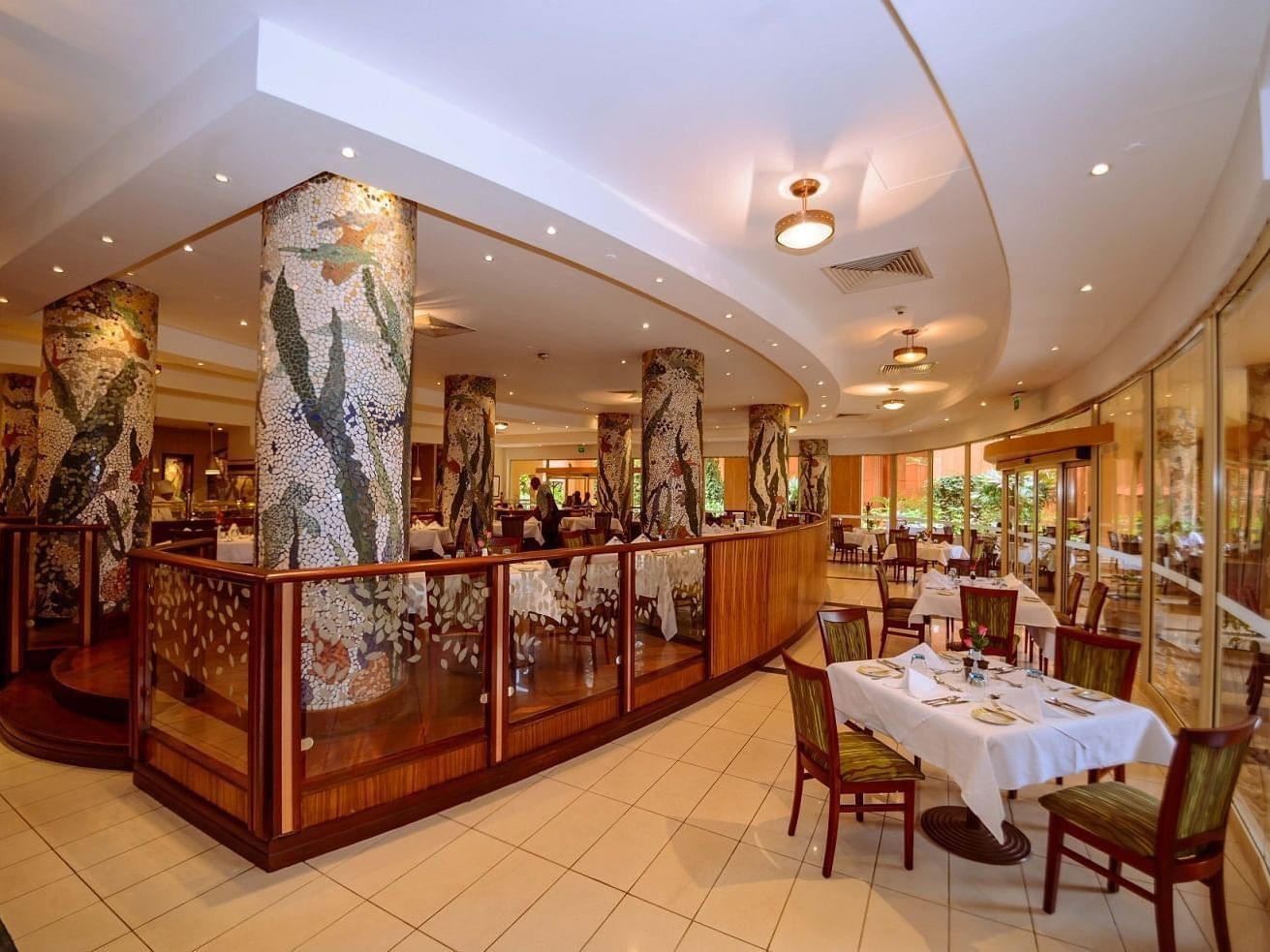 The Lakes Restaurant with mosaic pillars by glass railings under recessed lighting at Serena Resorts