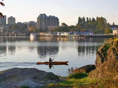 A kayaker paddles across a calm lake with city skyline in the background at sunset.