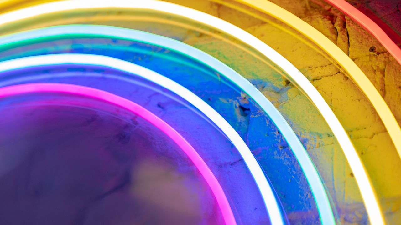 Colorful neon light strips forming a rainbow arc against a textured yellow wall creating a vibrant night light display.