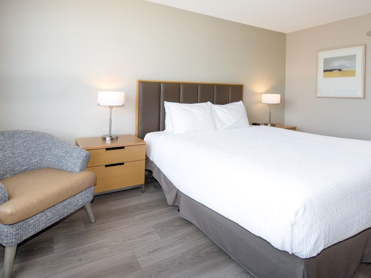 A hotel room with a large king bed, lamps, nightstands, a chair, and a framed picture.