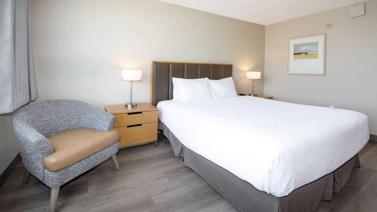 A hotel room with a large king bed, lamps, nightstands, a chair, and a framed picture.