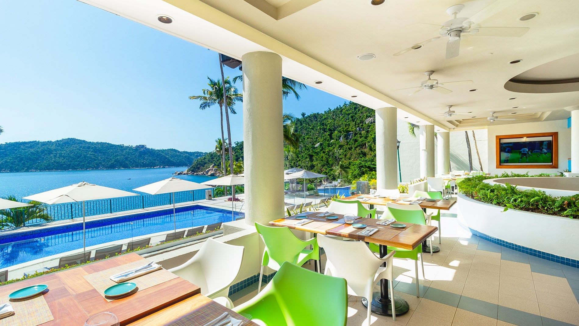 Open-air dining area featuring green chairs and a seaside pool at the Pool Bar in Camino Real Acapulco Diamante