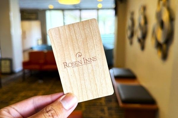A close-up of a hand holding a wooden Rosen Inns room key.