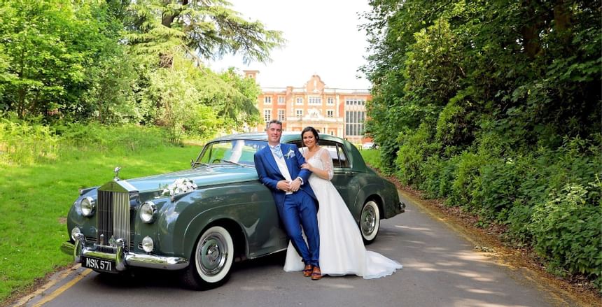 Newlyweds stand by the antique car at Easthampstead Park Hotel