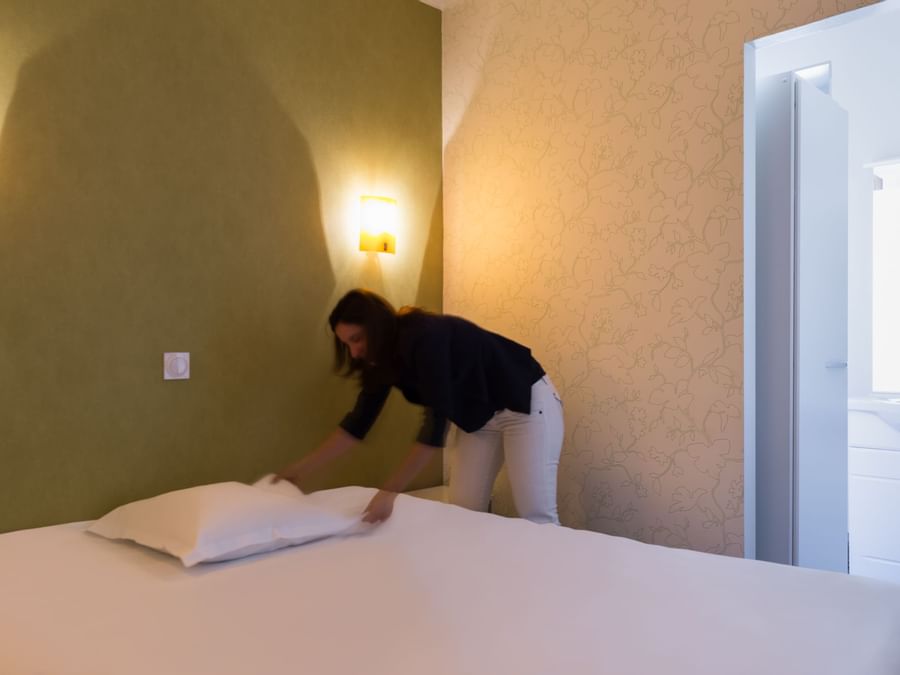 A lady preparing bed at Hotel Figeac