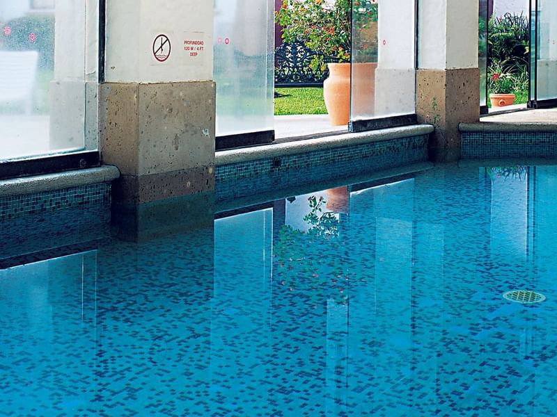 Indoor swimming pool with clear blue water and windows overlooking lush greenery view at Fiesta Inn Hotels