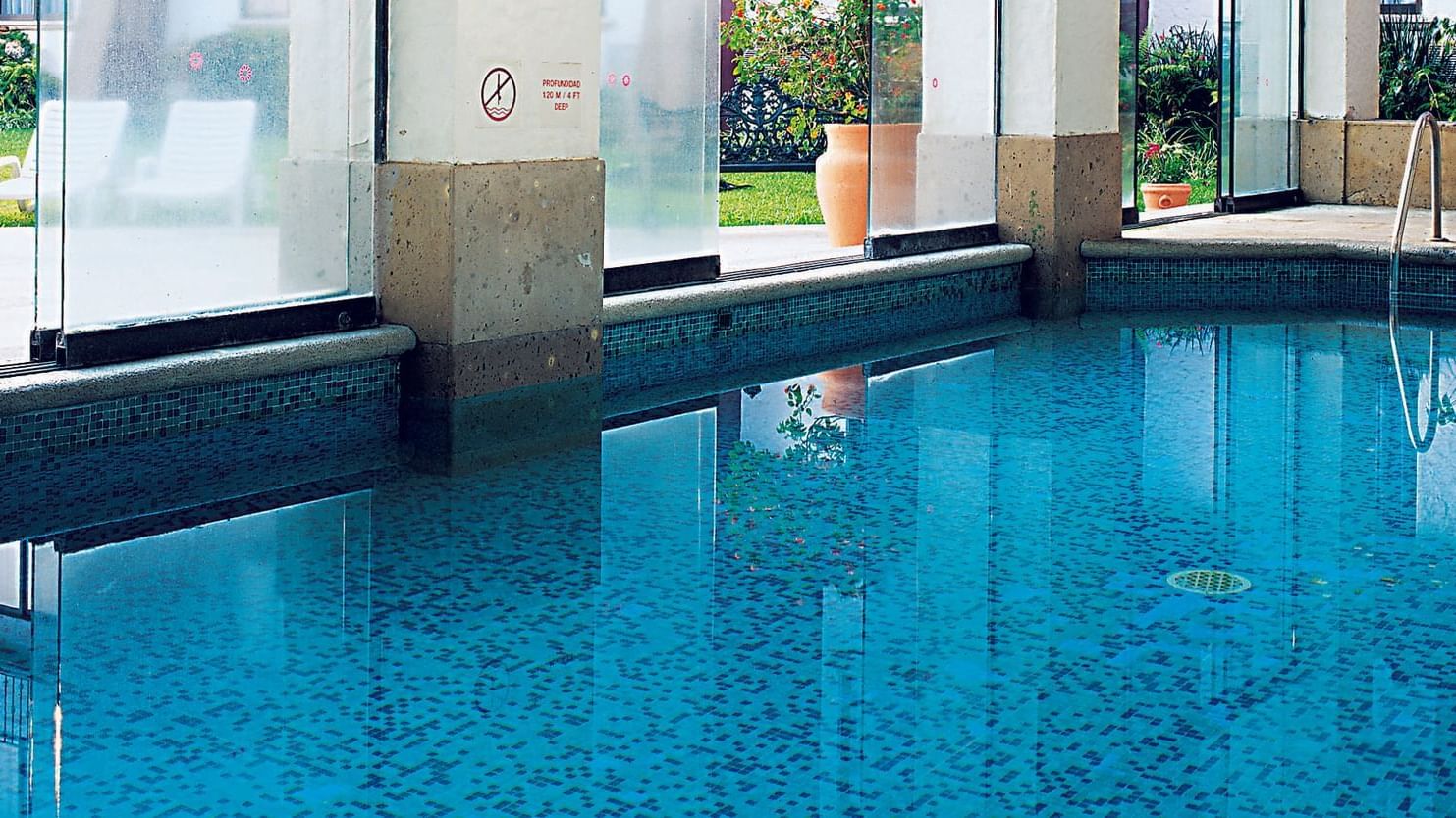 Indoor swimming pool with transparent windows overlooking the lawn area at Fiesta Inn Xalapa