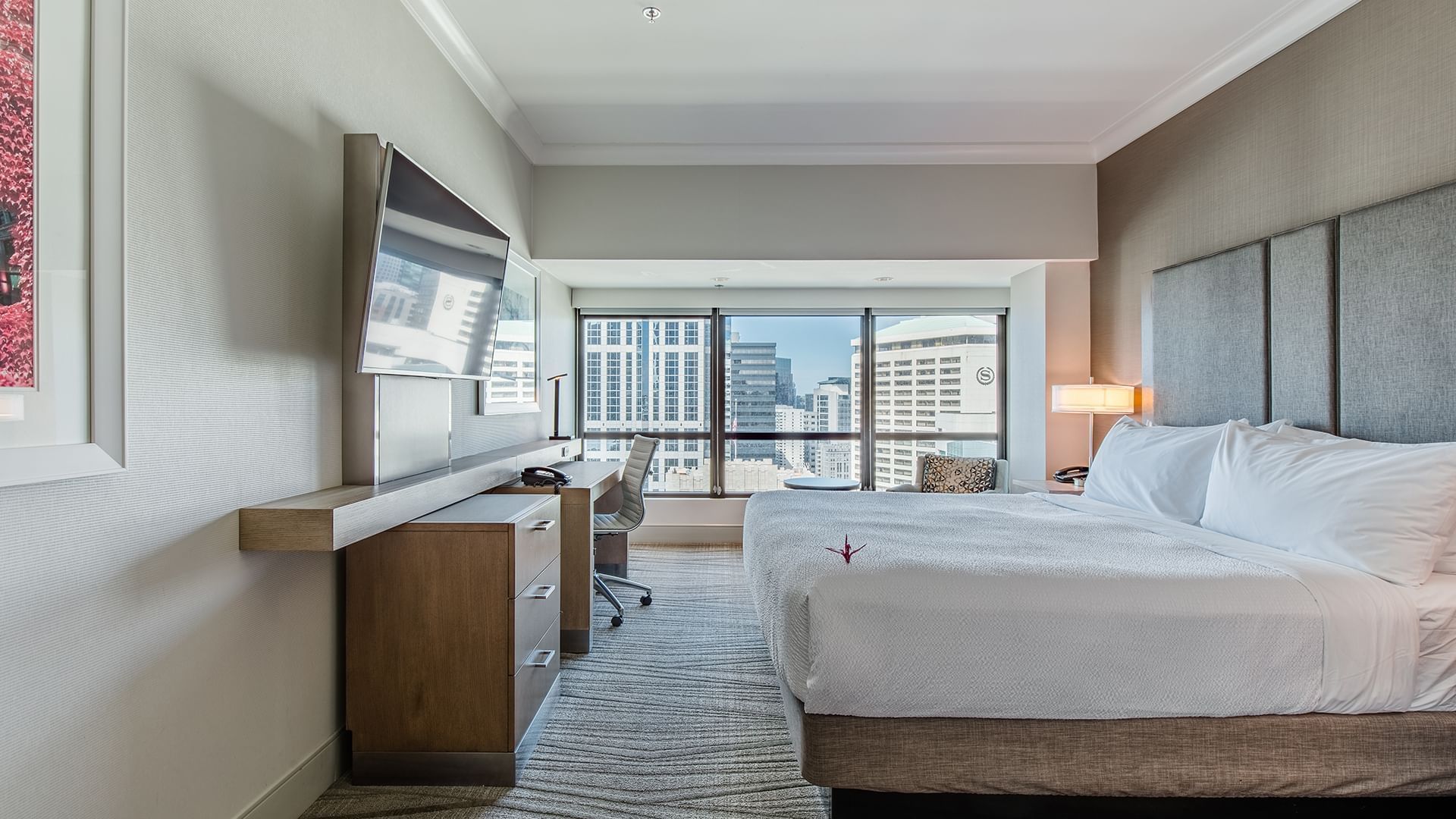 A hotel room with a king-size bed, desk, and city view.