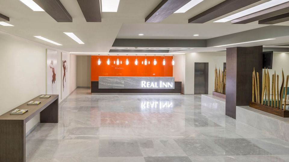 Modern reception desk featuring a vibrant orange wall and sleek marble tile flooring at Real Inn Celaya