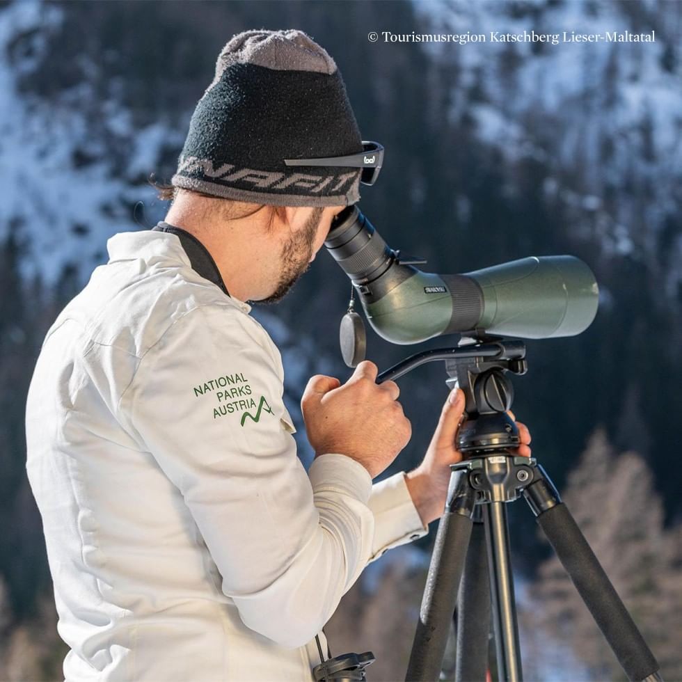 Man using binoculars on tripod during Wildlife Watching on Snowshoes at Maltaberg.