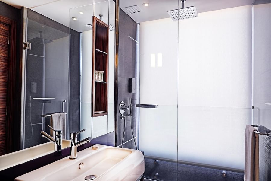 White sink by a glass shower stall and large mirror under a square showerhead in Deluxe Room at Warwick Stone 55 - Beirut