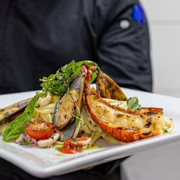 Chef holding seafood pasta with lobster tail and mussels for Interactive Cooking Demo at Sugar Cane Club Hotel & Spa