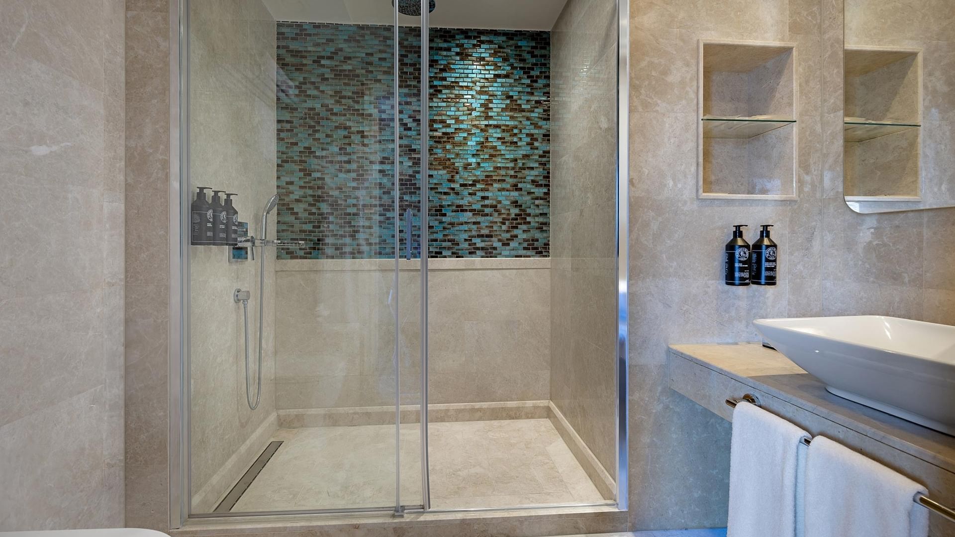 Titanic City Taksim'deki deluxe odanın banyosunda cam duşakabin, havlu ve lavabo görülüyor.