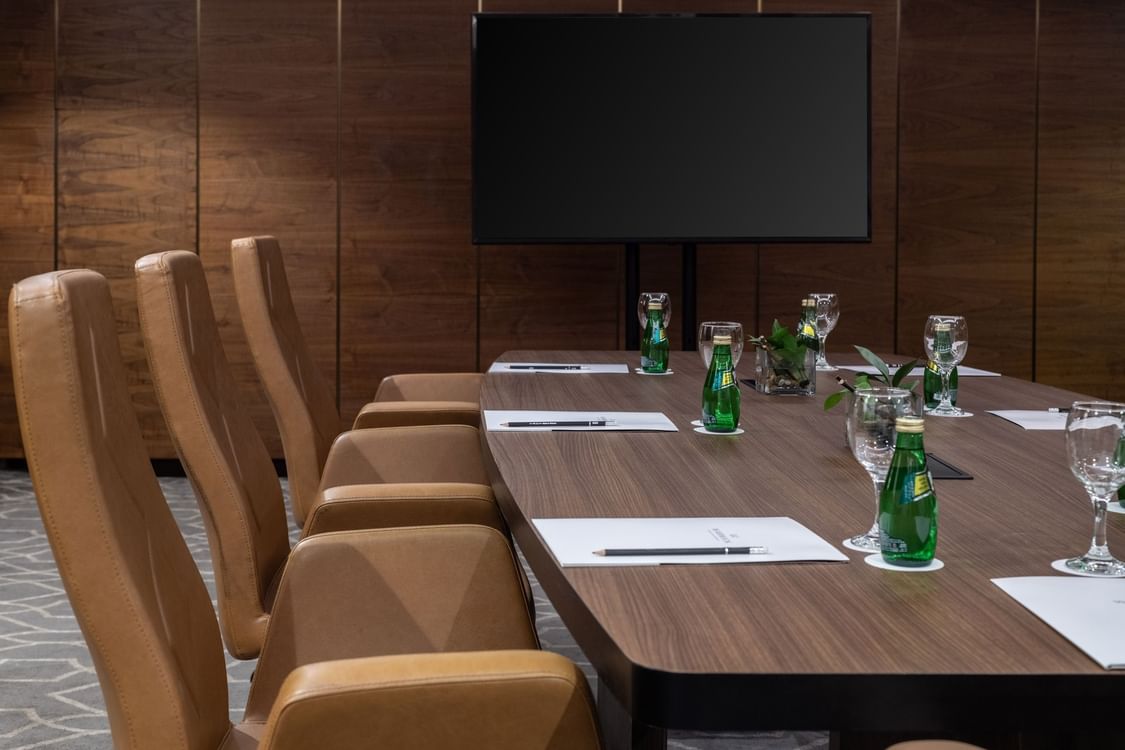 Meeting room with a large wooden table set with notepads, green bottles, and glasses at Warwick Hotel Jeddah