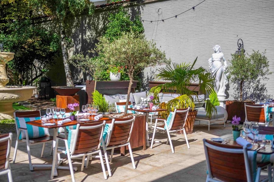 Al fresco dining on the sunlit garden terrace with white statues at Hotel Barsey by Warwick