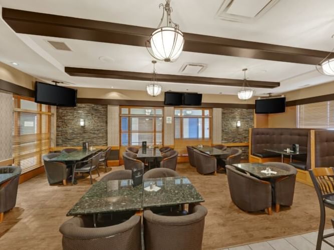 Dining table arrangements with TVs and chandeliers in illuminated Elbow Room Lounge at The Glenmore Inn & Convention Centre