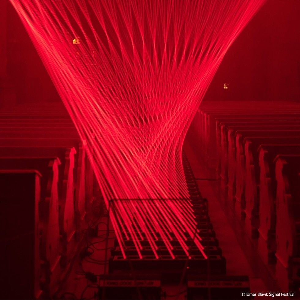 Red laser beams form a complex pattern in a dark room with rows of benches.