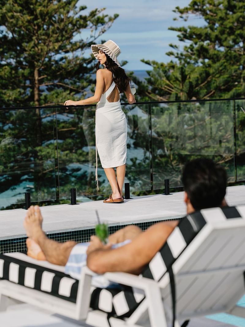 Woman at Elysium Manly standing in a white wrap by a glass pool fence to overlook pine trees, a top-choice hotel in Manly