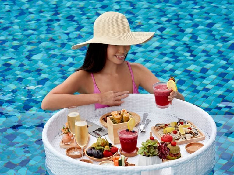 Women with a tray of appetizer in a pool by Verandah Pool Bar & Grill at Momentus Hotel Alexandra