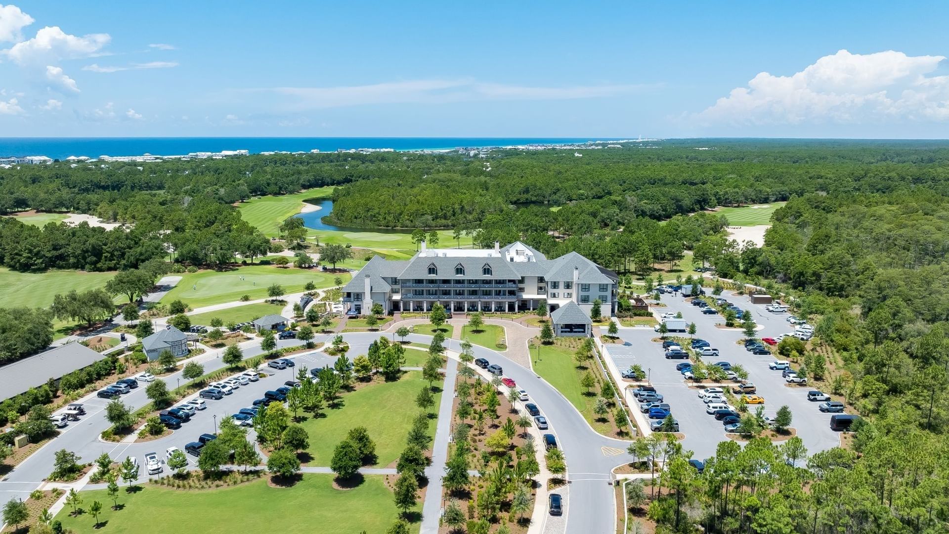 Aerial view of Fairway Park with white clubhouse, parking areas, and golf course near the ocean at Camp Creek Inn, Inlet Beach.