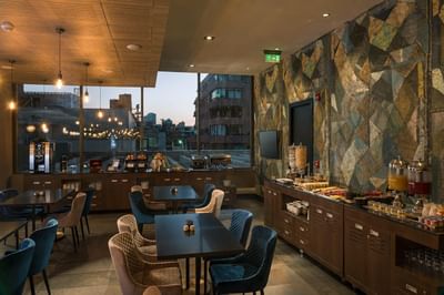 Veranda Restaurant dining area featuring tables & a breakfast buffet counter overlooking city buildings at Veranda Hotel