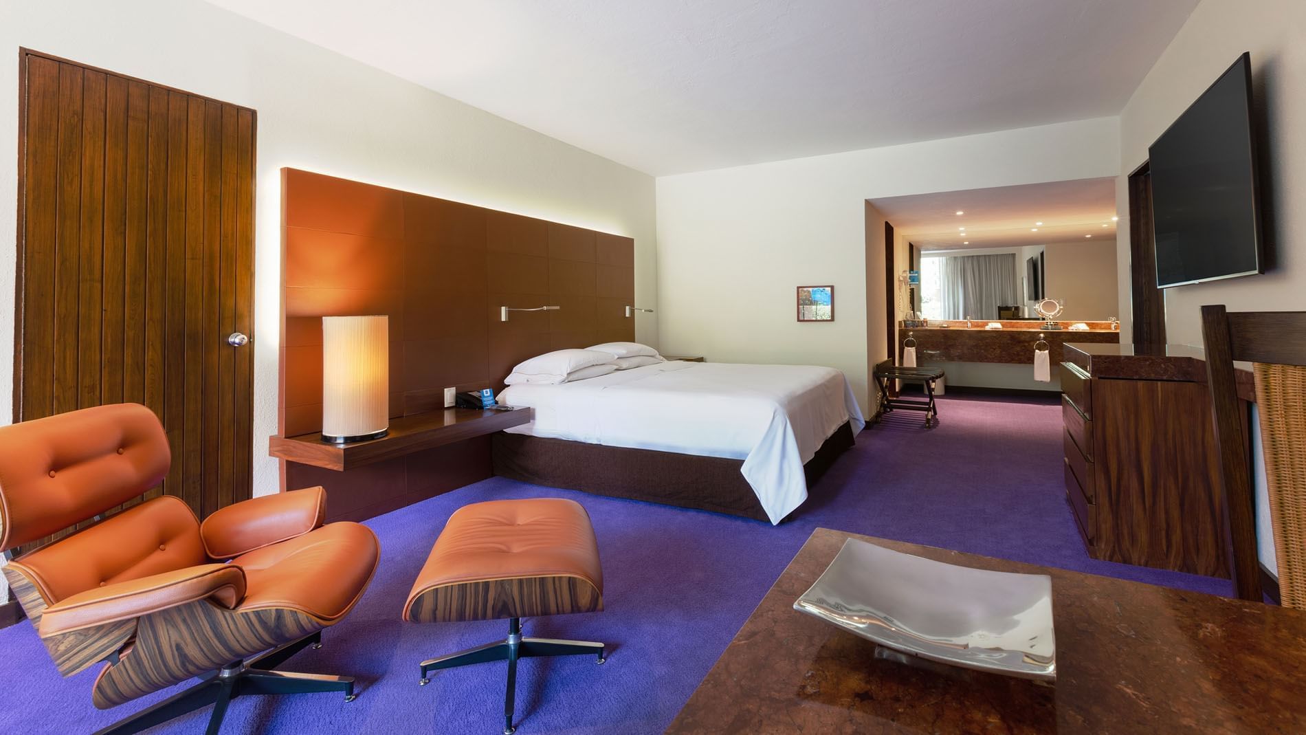 King Master Suite with a brown wood headboard, leather chair, and purple rug at Camino Real Polanco Mexico