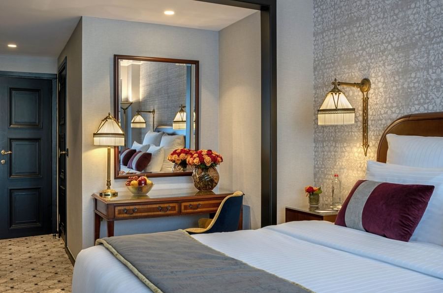 Wooden desk with a lamp & flower vase and mirror under a warm ceiling light in Deluxe Room at Hotel Barsey by Warwick