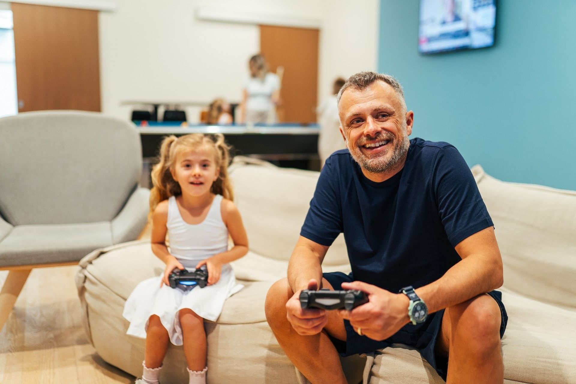 Father and young daughter smiling on a lounge couch with video game controllers in hand at Hotel X Toronto