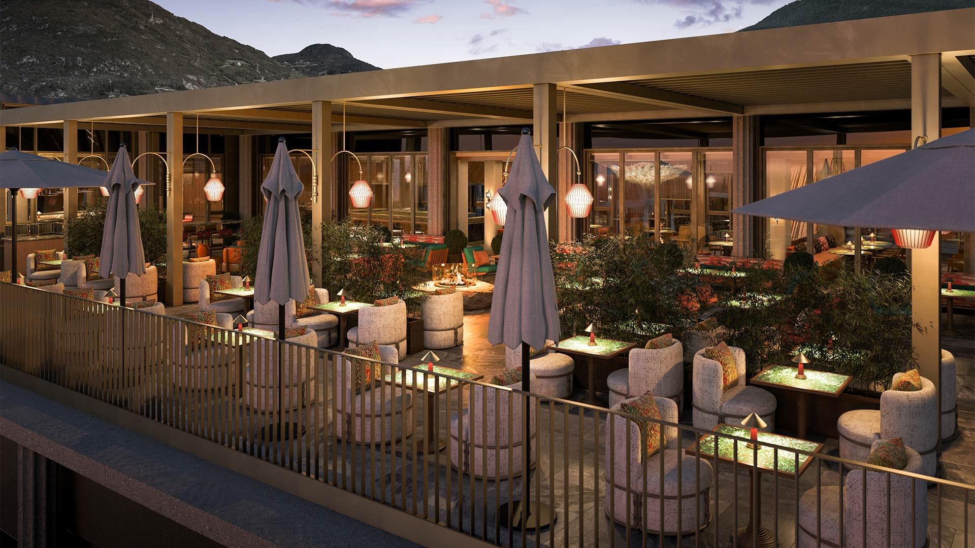 Außenterrasse eines Restaurants mit Möbeln, Pflanzen, Sonnenschirmen und Bergblick im Hintergrund.