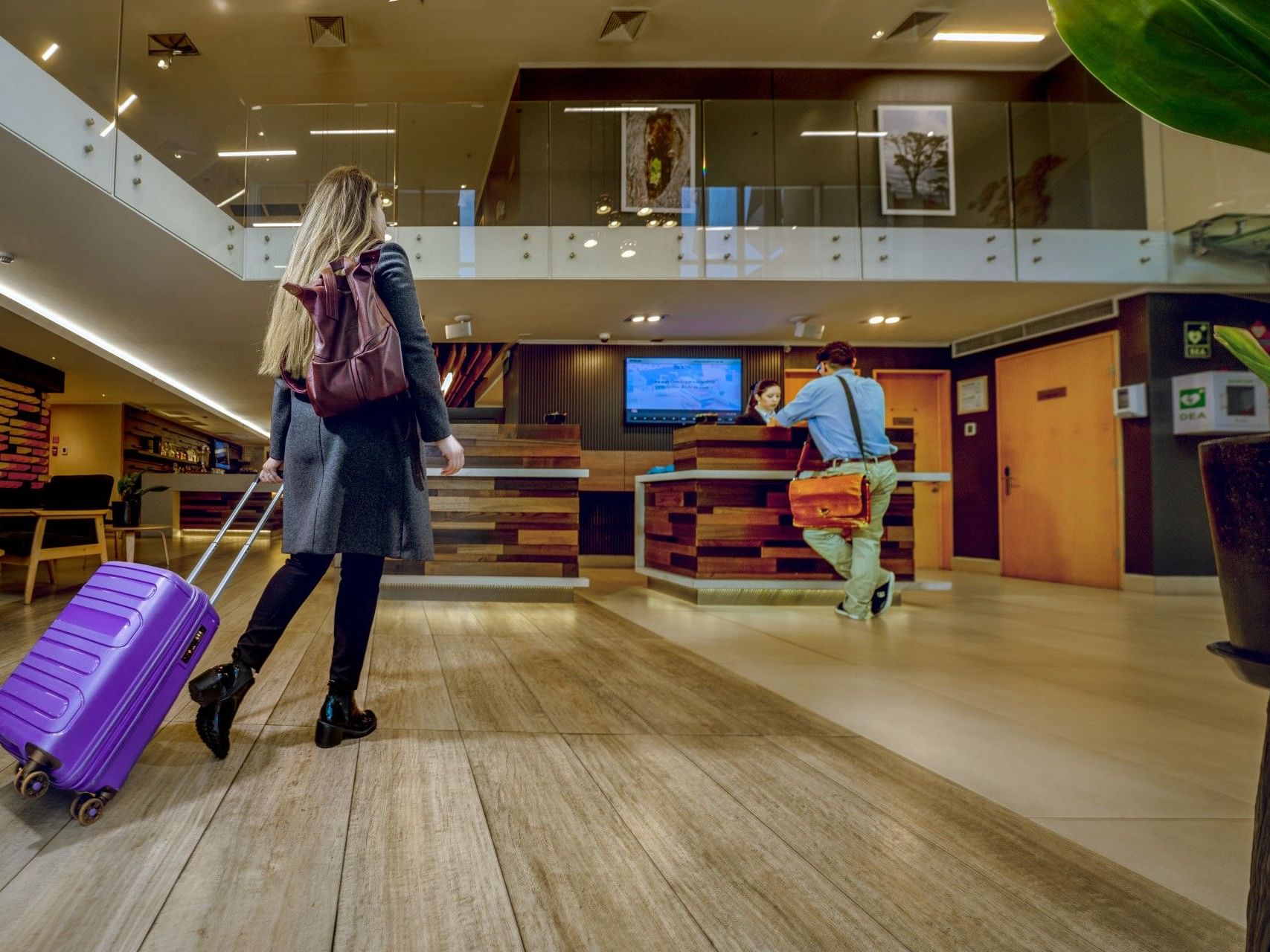 Mujer con una maleta morada caminando por el vestíbulo del hotel HCC Costanera Concepción.