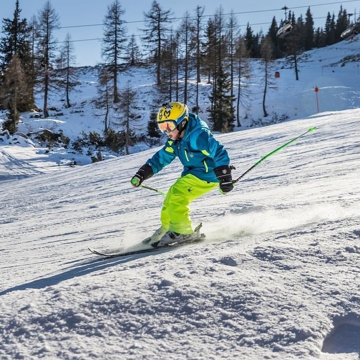Skifahrer in voller Ausrüstung fährt einen schneebedeckten Hang hinunter bei Falkensteiner Group