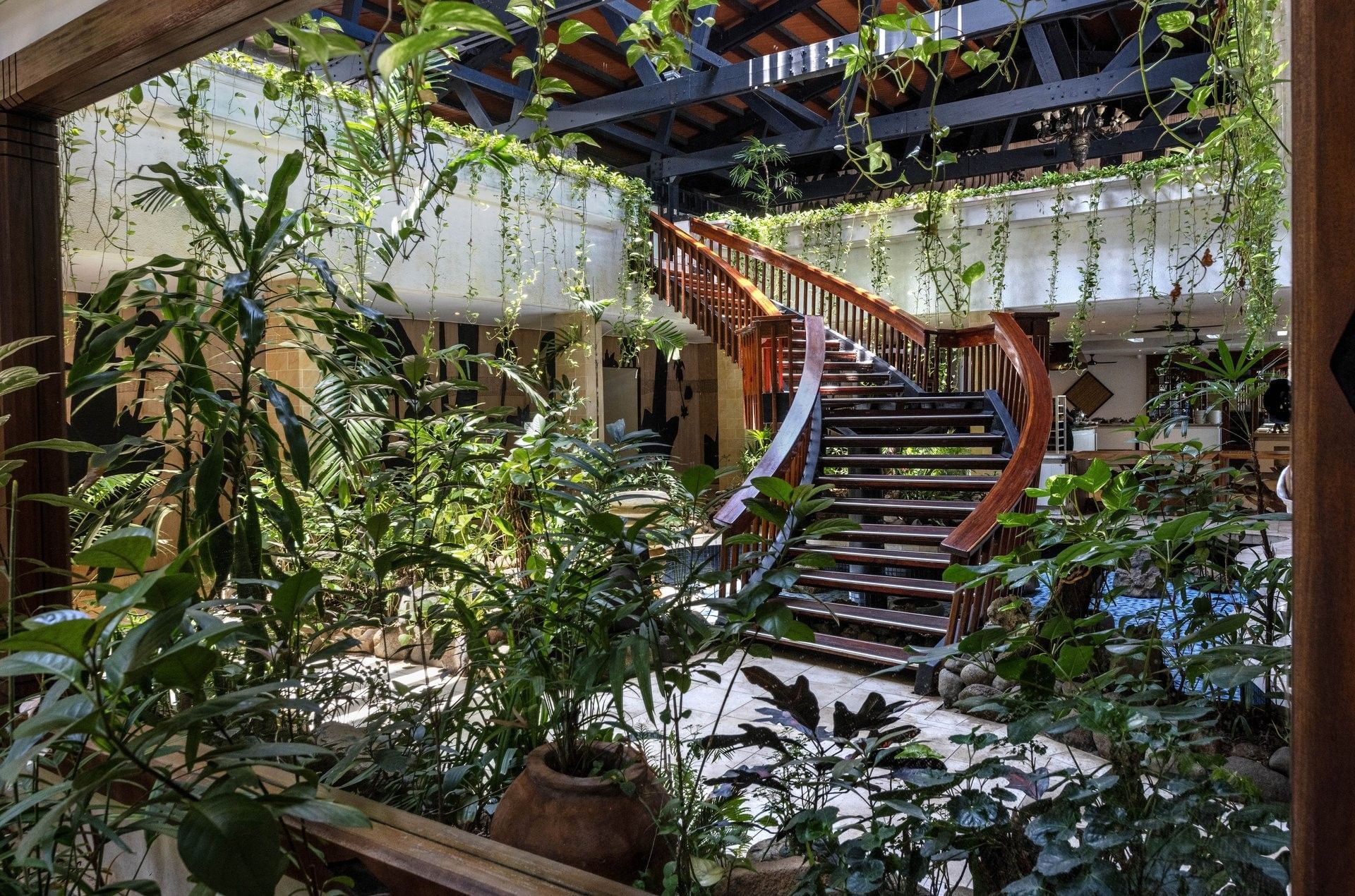 Spiral wood staircase by lush vines under a dark beamed ceiling at Warwick Fiji Resort and Spa