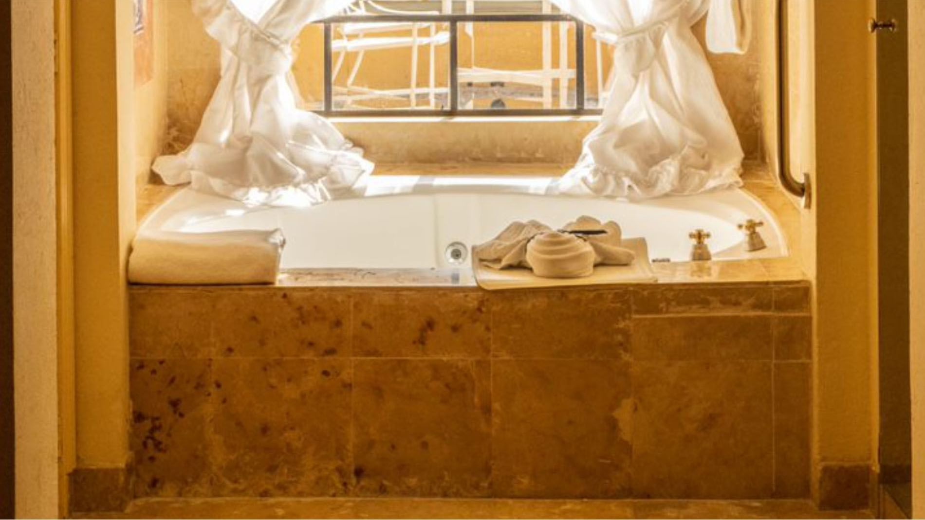 Marble bathtub in King Presidential Suite featuring white ruffled curtains and a bright window view at Quinta Real Monterrey