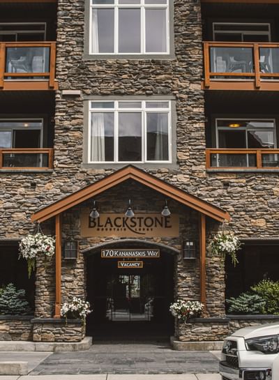 Blackstone Mountain Lodge entrance with stone walls, wooden canopy, and hanging flowers creating a warm welcome