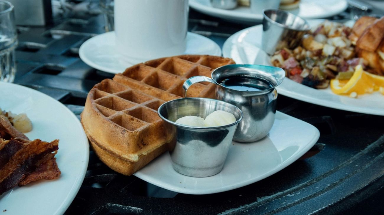 A waffle with syrup and butter in silver containers, part of a brunch setting served at The Grove Resort & Water Park