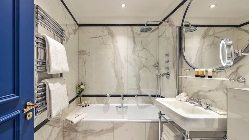 Modern bathroom featuring marble walls, a bathtub, towels on a rack in Superior room at Hôtel Westminster - Paris