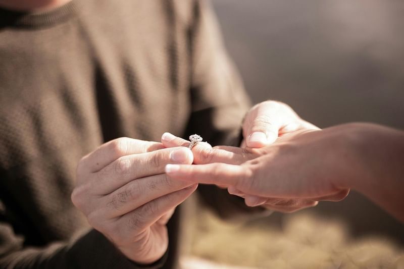 Close-up of a man's hands placing a diamond engagement ring on a woman's finger outdoors at Shangri-La Resort and Golf Club