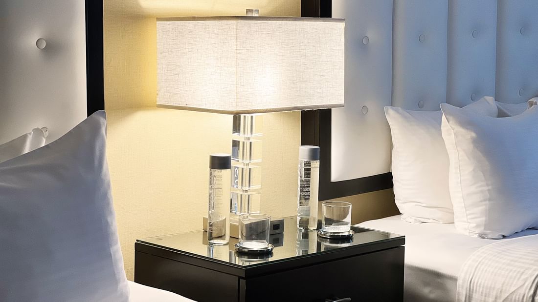 Close-up of beds with table lamp on side table in Premium Suite Two Queen Beds at Warwick Allerton Chicago