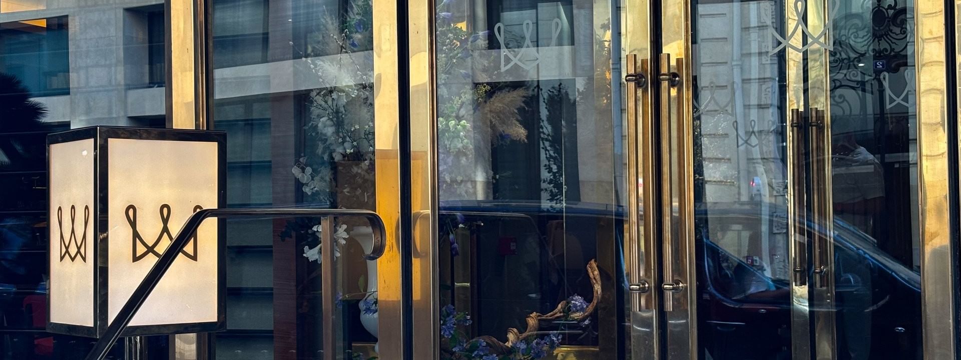 Glass doors by a square lamp under a blue sky reflecting the street view at Warwick Paris Champs Elysées