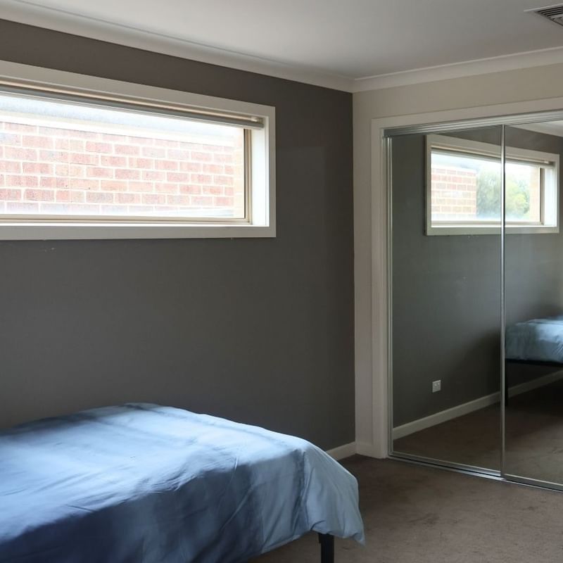 Bedroom with blue bed, large window, and sliding mirror door at La Trobe University Regional Housing – Melton.