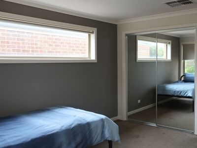 Bedroom with blue bed, large window, and sliding mirror door at La Trobe University Regional Housing – Melton.