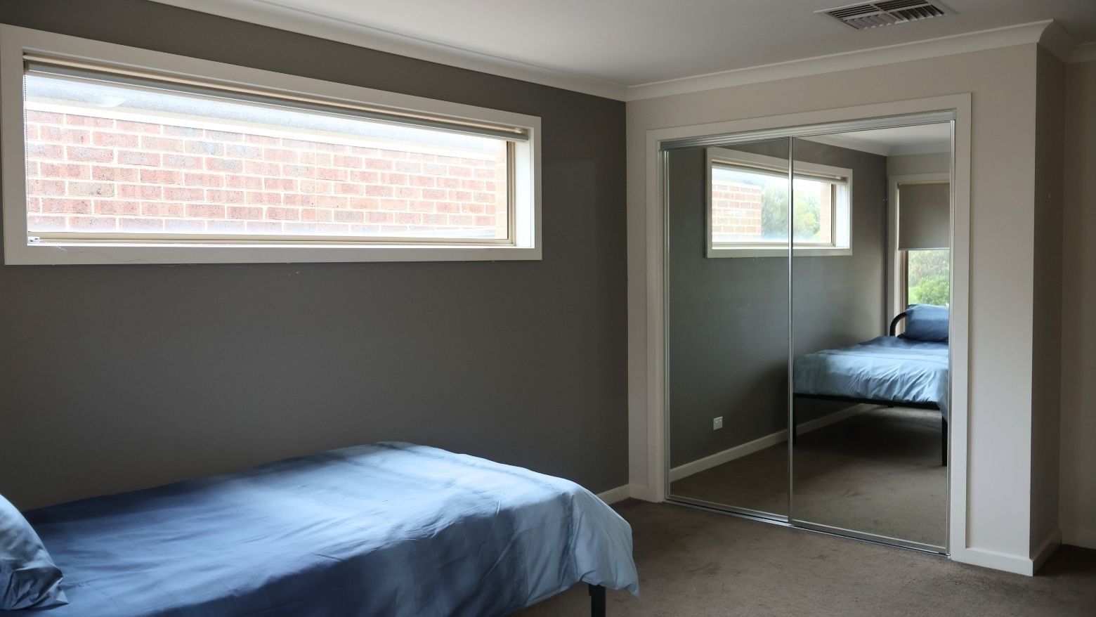 Bedroom with blue bed, large window, and sliding mirror door at La Trobe University Regional Housing – Melton.