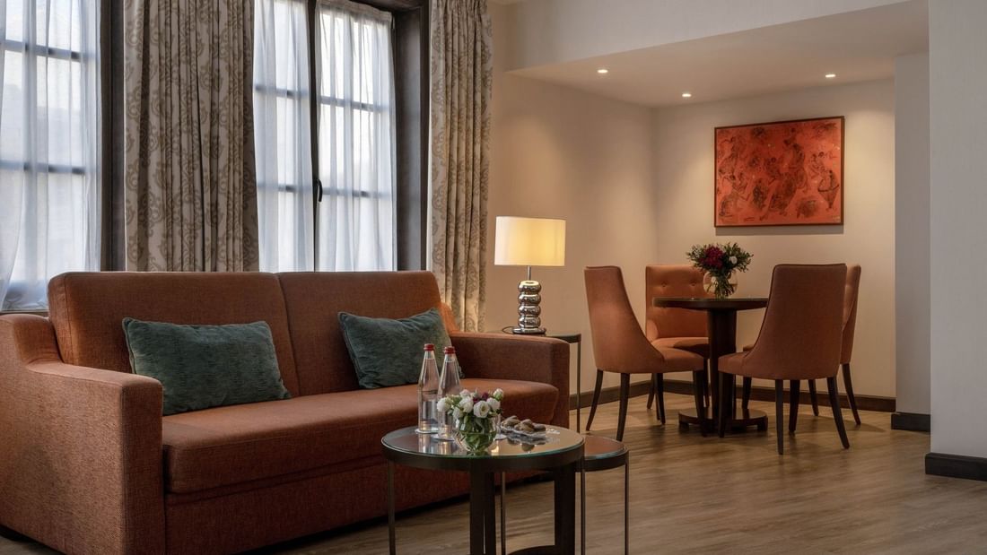 Un coin salon confortable avec canapé, table basse et coin repas dans la Junior Suite Privilege View du Warwick Grand-Place Brussels.