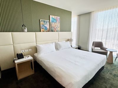 Bed with a cozy armchair by large windows and wall-mounted artwork in Duet Deluxe at Encore By Mingara