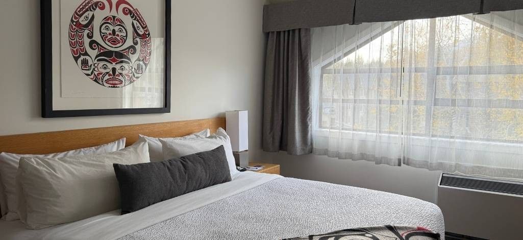 Guest room with king bed, framed Indigenous artwork, and large window.