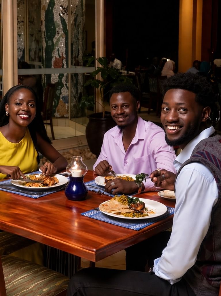Three guests smiling during a candlelit dinner with traditional plated meals at Serena Hotels & Resorts