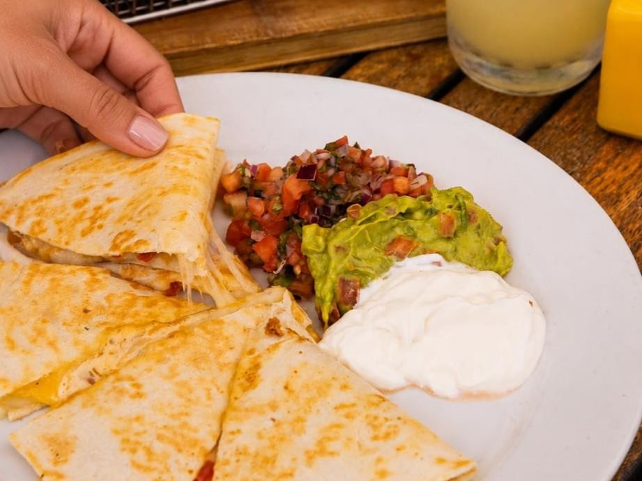 Grilled quesadillas served with salsa, guacamole, and sour cream alongside margaritas for National Quesadilla Day