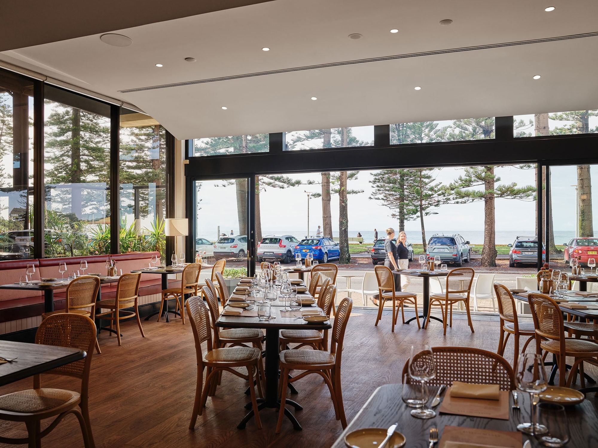 Bistro Manly at Elysium Manly featuring neatly set dining tables & woven chairs facing large glass windows right by the sea