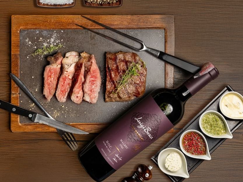  A bottle of wine beside a perfectly cooked steak on a wooden cutting board, showcasing a delightful dining experience.