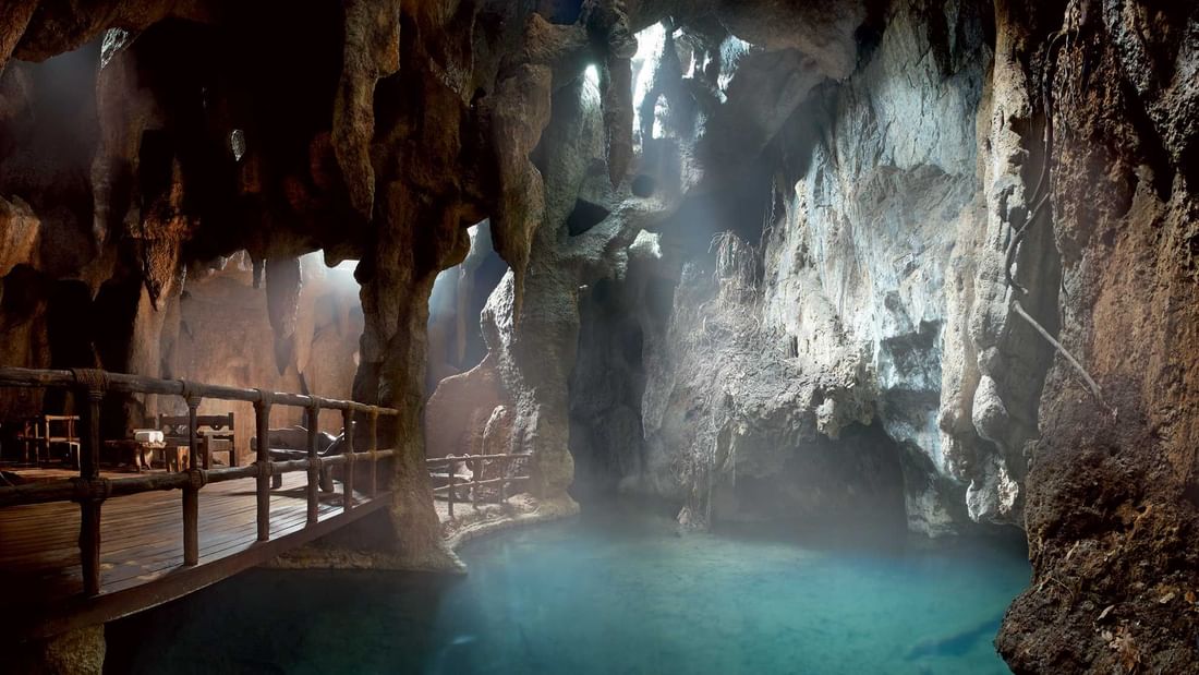 Treatment cave with a turquoise pool, wooden walkway, and natural rock formations at The Banjaran Hotsprings Retreat